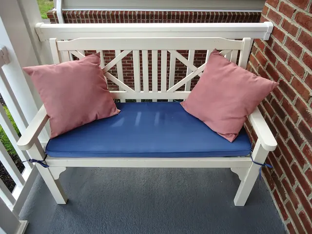 Two dusty-pink cushions at either end of a white garden bench with a blue seat pad.