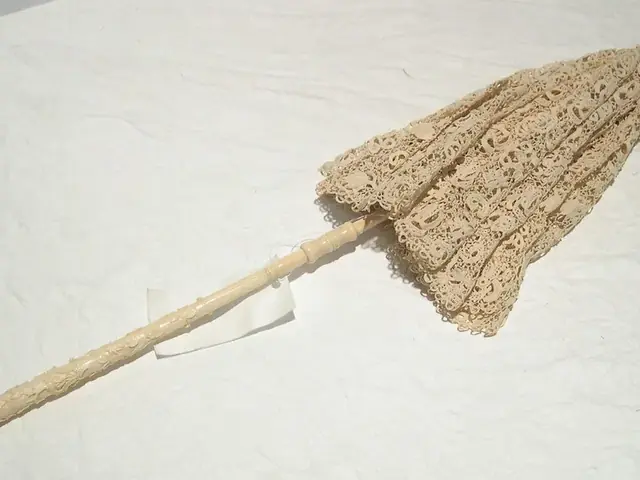 A cream lace parasol, closed, with a turned wooden handle lying on a white cloth.